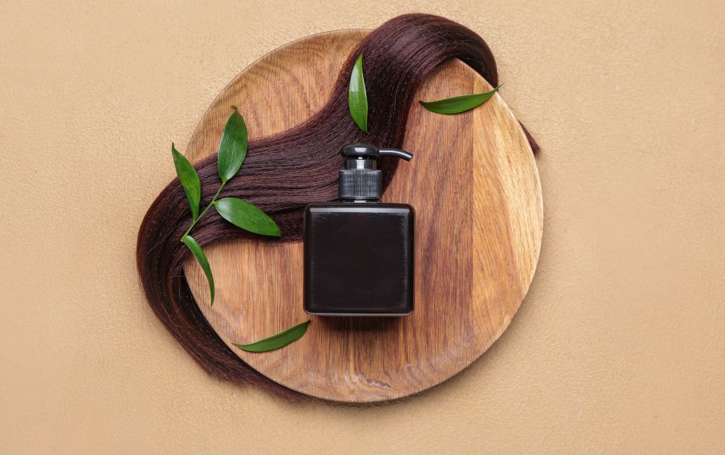 髪の毛と黒いパッケージに入ったヘアオイル。ヘアケアイメージ
